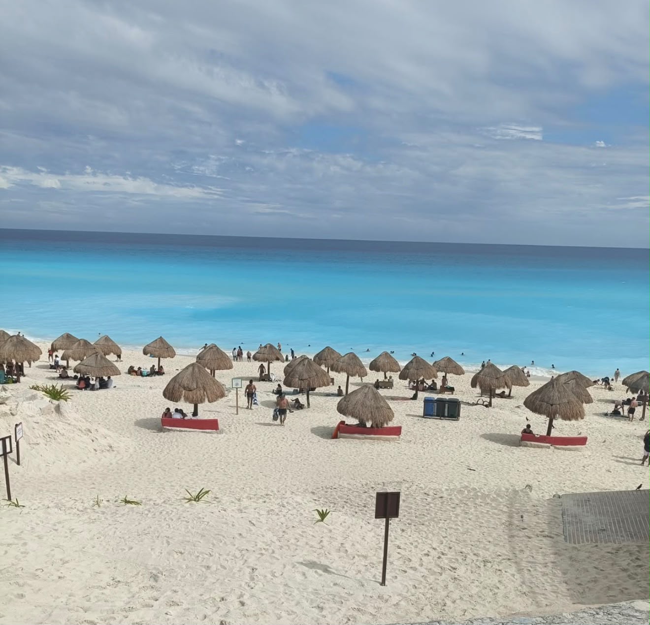Playa de Cancún con palapas de paja y mar turquesa, llena de visitantes
